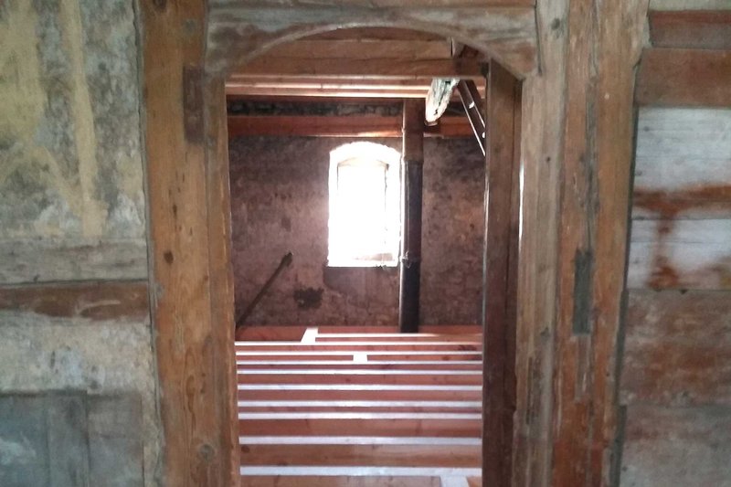 Hinter einem mit Holz umrahmtem Eingang ist ein alter Dachstuhl zu erkennen.