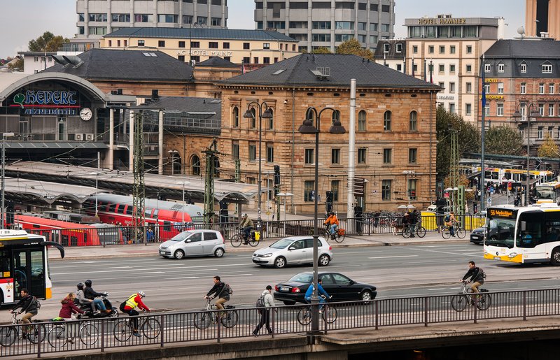 Blick auf den Mainzer Hauptbahnhof, davor Autos, Busse und Radfahrer, im Hintergrund Züge