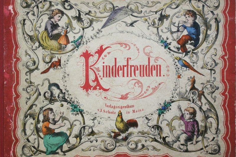 Zu sehen ist der Vorderdeckel eines alten Kinderbuchs des Verlags Jos. Scholz. Der Titel ist gezeichnet. Zu sehen sind Ranken sowie in jeder Ecke ein Kind, das Spielzeug in Händen hält. Dazwischen sind Tiere abgebildet.