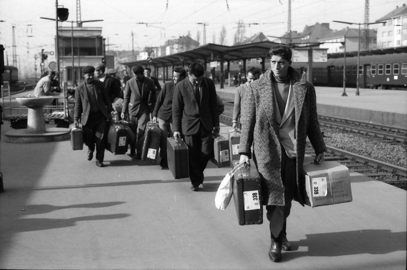 Schwarz-Weiß Fotografie. Männer mit Koffern an einem Bahnsteig.