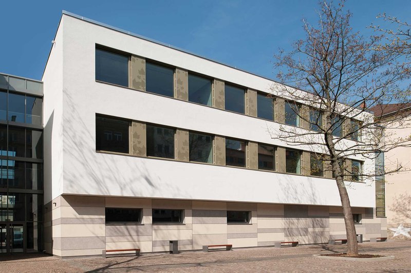 Das Frauenlob-Gymnasium ist zu sehen: Ein moderner, weißer Flachbau. Davor steht ein kahler Baum.