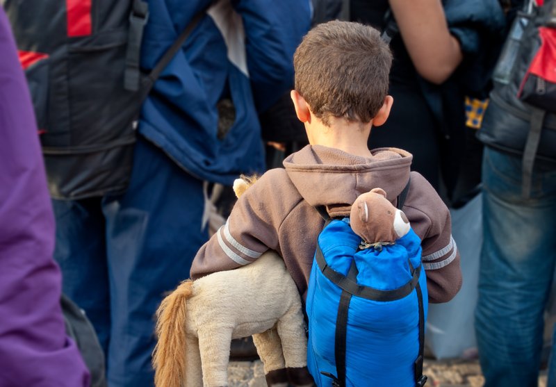 Ein Junge mit Rucksack und Kischeltier steht mit dem Rücken zur Kamera